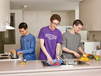 three young men prepping food together in their residence dorm, all laughing