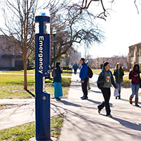 blue emergency phone in front of students walking on the sidewalk on campus