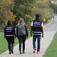 a student wearing a back pack walking in between two students with foot patrol vests