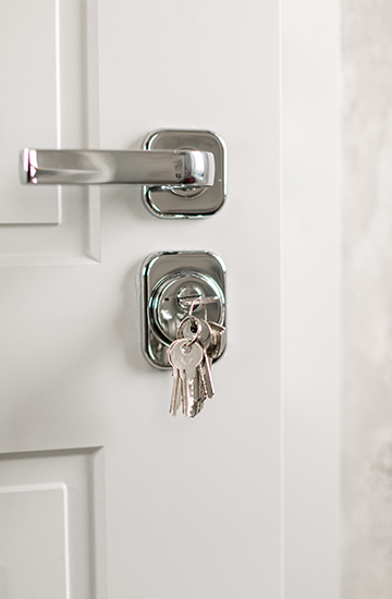 key hanging in lock of white door just below silver horizontal handle