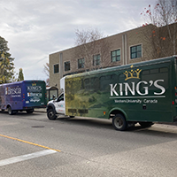 two long shuttle buses with the King's and Brescia logos parked in front of a university building