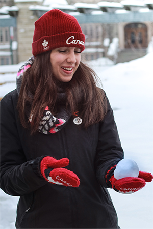 Student wearing warm winter gear holding a snowball in her gloved hand and smiling.